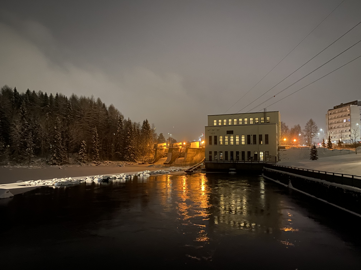 Koivukoski II voimalaitos näkyy valaistuna pimeässä ja lumisessa maisemassa Kajaanijoen varrella.